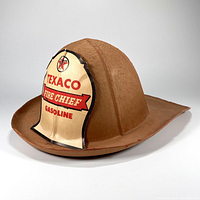 Side angled view of vintage Texaco Gasoline child's fire chief helmet showing detailed badge and curved brim