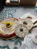 Photo showing multiple paper lanterns stacked together on carpet, including large red-trimmed round and white circular lanterns, with wooden wall art pieces nearby.