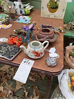 Various dragon figurines and other items on a table, including a ceramic teapot, brown resin bowl, and a dragon-themed compact or pocket watch.