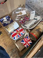 Image showing box of assorted British flag themed mugs, plates, a Union Jack bow tie and purse, a metal tin, and a decorative porcelain dish.
