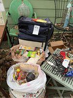 Overview of the fishing supplies collection showing the soft tackle case, assorted lures, fishing reels, and other fishing gear arranged on outdoor furniture.