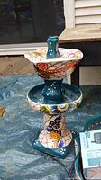 Full view of the ceramic two-tier Mexican fountain showing colorful floral hand-painted design and turquoise base, displayed outdoors.