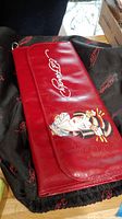 Red Ed Hardy purse with Geisha Girl artwork and Ed Hardy logo, resting on black Ed Hardy dust bag with red logos.