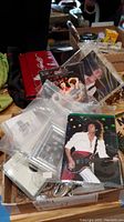 Box of assorted Queen band memorabilia including postcards, pins, pictures, and magnets in plastic sleeves and packaging.