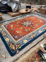 Full view of the rust orange and blue floral patterned wool rug laid on the ground, showing the overall design and condition including some light wear.