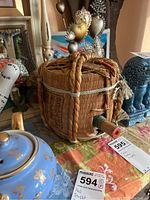 Side view of vintage sake bottle within a hexagonal woven wicker basket with braided rope handles and Japanese writing on the basket.