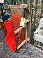 Side view of vintage Paris Company child sized wooden sled showing wooden frame, curved runners, and red fabric seat with straps.