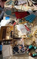 Overview of costume jewelry including bracelets, earrings, and watches spread on surface with fans in background.