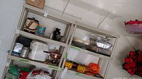 Metal shelves holding several kitchen and serving items including disposable pans, glass vases, plastic pumpkin themed containers, and other kitchen items.