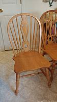 Single wooden dining chair with carved backrest showing the rounded top and cutout design in the central splat, turned legs visible