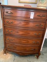 Frontal view of the chest of drawers showing all five drawers with curved fronts and metal handles, overall wood finish and design.