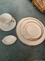 Photo showing a cup with a saucer, a small oval dish, and plates with silver trim edges