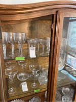 Photo of crystal glasses displayed in a wooden cabinet including wine glasses, champagne coupes, and small crystal plates.