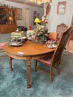 Oval wooden dining table in a carpeted room with chairs around it and various decorative items placed on top.