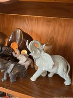 Shelf displaying variety of elephant figurines including white ceramic and dark stone elephants.