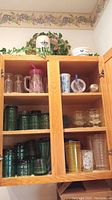 Kitchen cabinet shelf with glassware including vintage green tumblers, clear dessert glasses, ceramic tumbler, plastic cup, and stainless bottle.