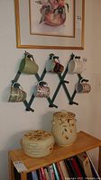 Full lot shot showing lidded pottery pieces on shelf and wooden mug rack with six mugs mounted on wall.