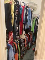 Wide view of the women's clothing hung in a walk-in closet showing pants, shirts, skirts, and dresses in multiple colors and prints.