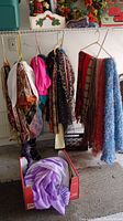 Scarves and belts hanging on a rod, various colors and styles including animal print, bright pink, and blue textured knit.