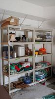 View showing two plastic shelving units side by side with various household items on shelves; shows general condition and visible damage to bottom shelves.