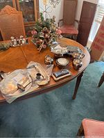 Full overview of table displaying silver plate serving pieces, including ladles, dishes, creamers, and condiment containers on a wood dining table.