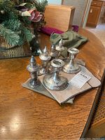 Six piece sterling silver set including two candle holders and four salt and pepper shakers arranged on a cloth on a wooden table.