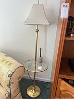 Full view of brass floor lamp with glass tabletop and canvas shade next to a couch