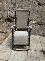 Front view of beige zero gravity chair with pillow, metal frame with rust, and gray plastic armrests on patio