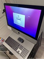 Front view of iMac powered on showing setup screen with keyboard and mouse in foreground