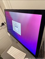 Side front angle view of iMac powered on displaying macOS setup screen, with Magic Keyboard and Magic Mouse visible.