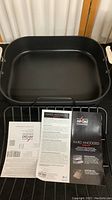 Photo of All-Clad roaster pan interior, rack, and instructional leaflets.