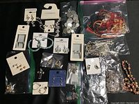Top view of assorted earrings, some on branded cards, loose chains, bracelets, and small jewelry pieces in bags against black background