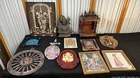 Full view of eleven items on a black fabric display including framed artworks, wooden temple, deity sculptures, and decorative pieces
