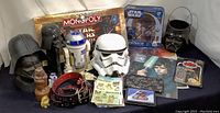 Wide shot showing multiple Star Wars collectibles including masks, figures, Monopoly game, belts, posters, and other memorabilia on a black background.