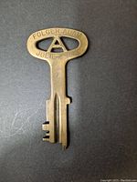 Photo of the front side of the solid brass key showing 'FOLGER ADAM JOLIET, ILL' engraving and the unique 'A' cutout in the handle.