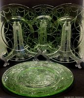 Set of four green depression glass dinner plates displayed on stands, showing embossed ballerina and decorative garland patterns.