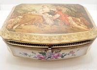 Front angled view showing hand-painted Victorian couple scene on lid with surrounding gold trim and floral design on the front of the porcelain box. Metal clasp visible.