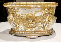 Front view of painted terracotta planter showing distressed silver and gold finish with cherub head and wing decoration.