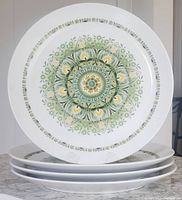 Stack of four Noritake Progression China plates with green and yellow floral geometric design on white background.