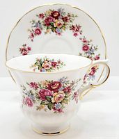 Front view of Paragon tea cup with floral flower festival pattern and matching saucer behind, showing gold rims and decorative handle.