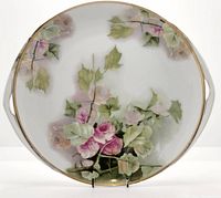 Front view of charger plate showing floral hand painted design, gold trim, and side handles.