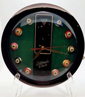 Front view of the vintage billiards-themed clock, showing black frame, green felt background, billiard ball hour markers, and clock hands.