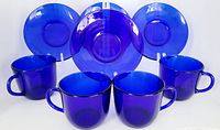 Four cobalt blue glass cups and four matching saucers arranged with cups in front and saucers behind, showing color and shape.