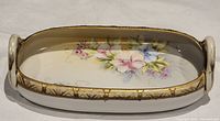 Full view of the oval Nippon trinket dish with two handles and floral hand painting with gilt border.