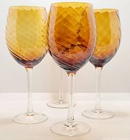 Four amber swirl handblown wine goblets shown from front and slightly angled to show texture and pattern of amber swirl on glass bowls with clear stems and bases.