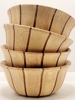 Stacked set of four round salad bowls showing the vertical dark teak stripes contrasting pale beech wood.