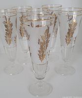 Set of six frosted pilsner glasses with gold-tone leaf designs and gold banding around the rim and base of the bowl, on clear stemmed bases.