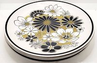 Stack of four vintage Mikasa Cera-Stone Leilani dinner plates showing floral black, white, and gold flower pattern with black rim.