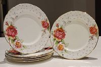Six vintage Paragon bread plates stacked and two displayed upright, showing floral designs and gold-rimmed scalloped edges.