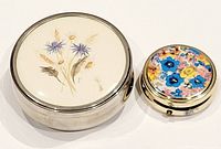 Two round vintage boxes, one larger trinket box with floral top, one smaller colorful enamel pill box